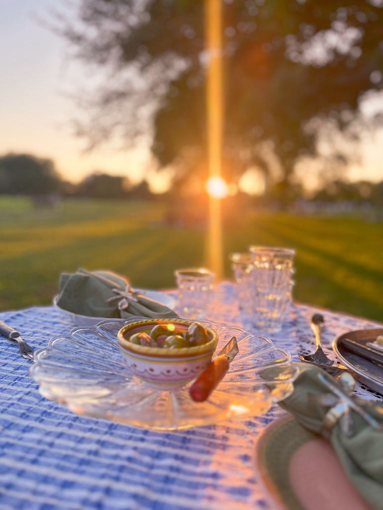 a table set for dinner in the park with the sun setting in the background