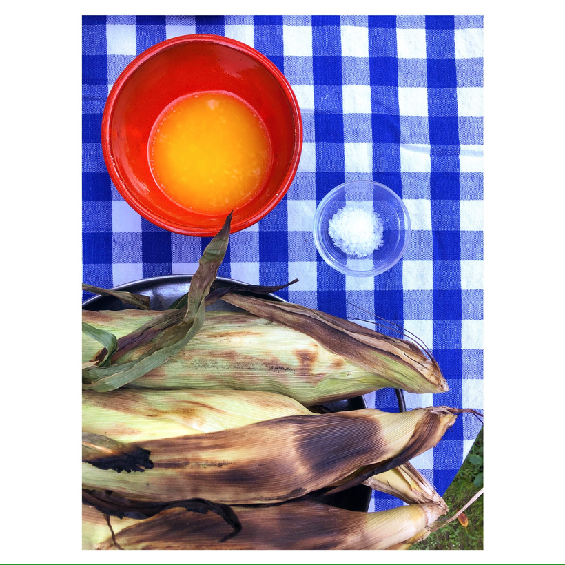 ears of corn and a red bowl of butter on a blue and white tablecloth
