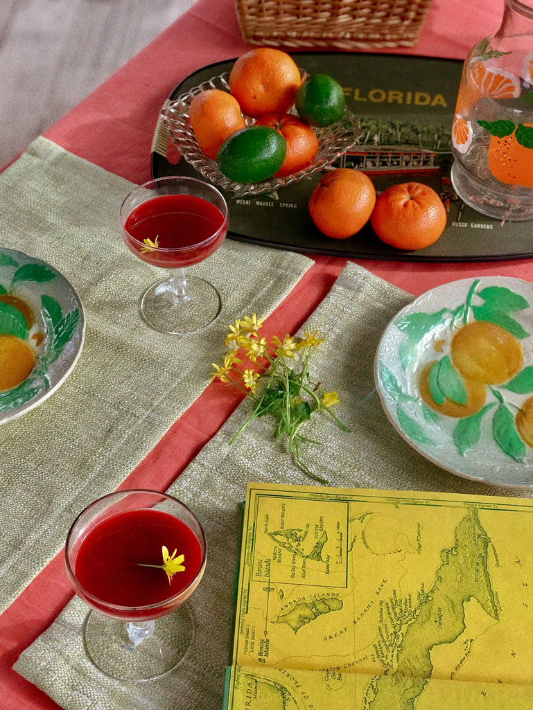 a table topped with red juice, oranges, flowers and a map of florida