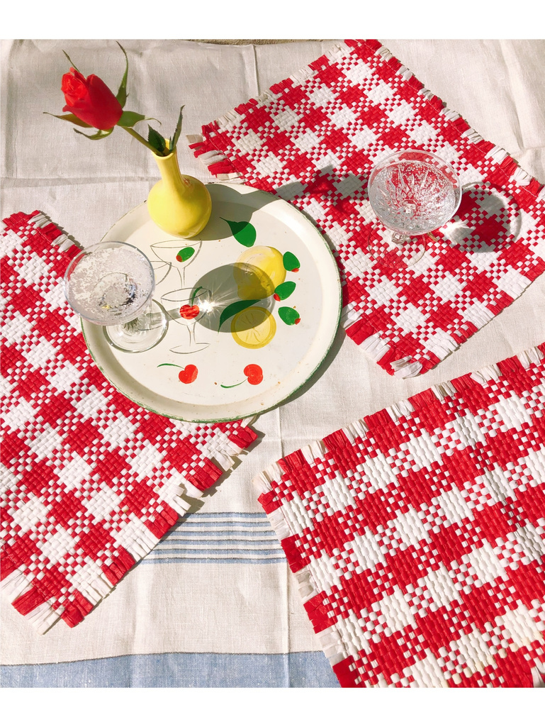 a table with red and white checkered placemats, a champagne glass and a rose in a yellow vase on a decorative tray.