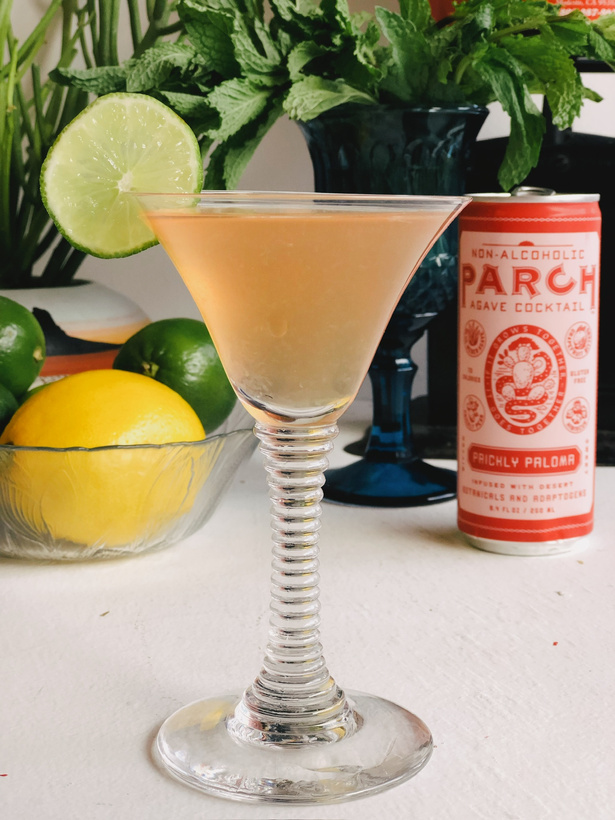 a cocktail in a martini glass next to a can of Parch cocktail and a bowl of lemons and limes.