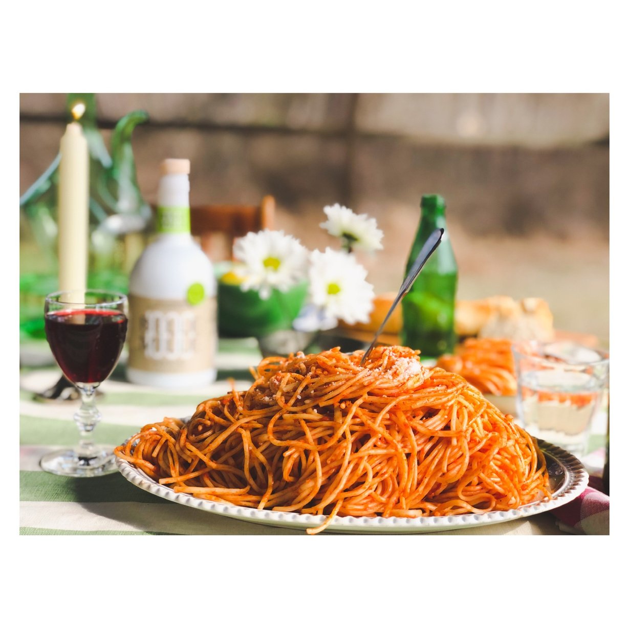 spaghetti with red sauce on a plate and a glass of red wine on the table