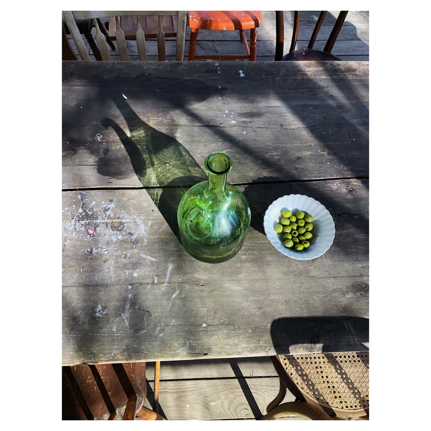 a wooden table with a green vase and a bowl of olives