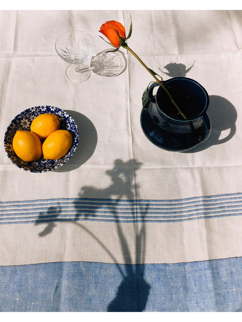 a blue and white striped tablecloth with a bowl of lemons and a cup of tea